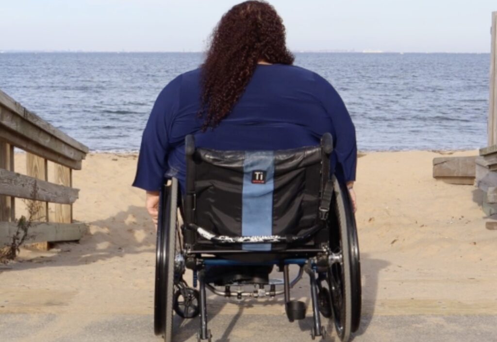 a woman in a wheelchair faces the ocean along the beach