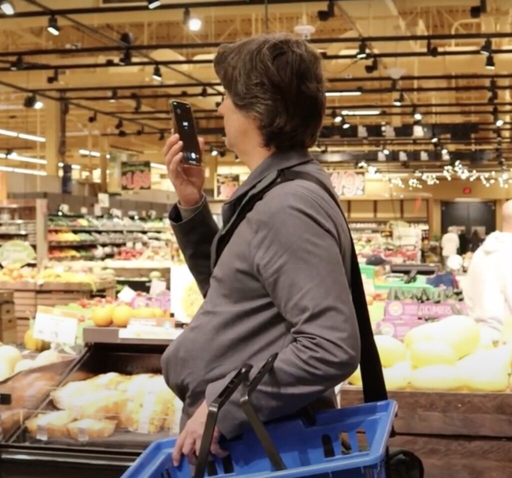a man holds a smartphone at eye level inside a supermarket