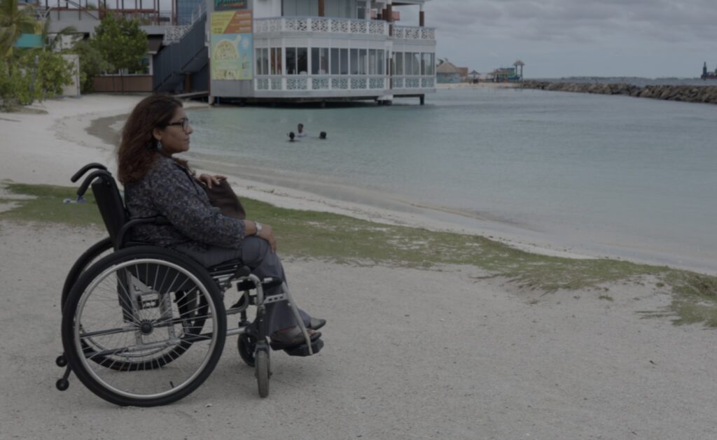 A woman sitting in a manual wheelchair looks out toward a harbor.